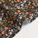 Digital printed cotton voile meadow of small green and orange flowers on a black background