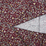 Cotton poplin printed with sprigs of mistletoe and gold stars on a wine-colored background