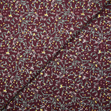 Cotton poplin printed with sprigs of mistletoe and gold stars on a wine-colored background