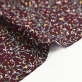 Cotton poplin printed with sprigs of mistletoe and gold stars on a wine-colored background